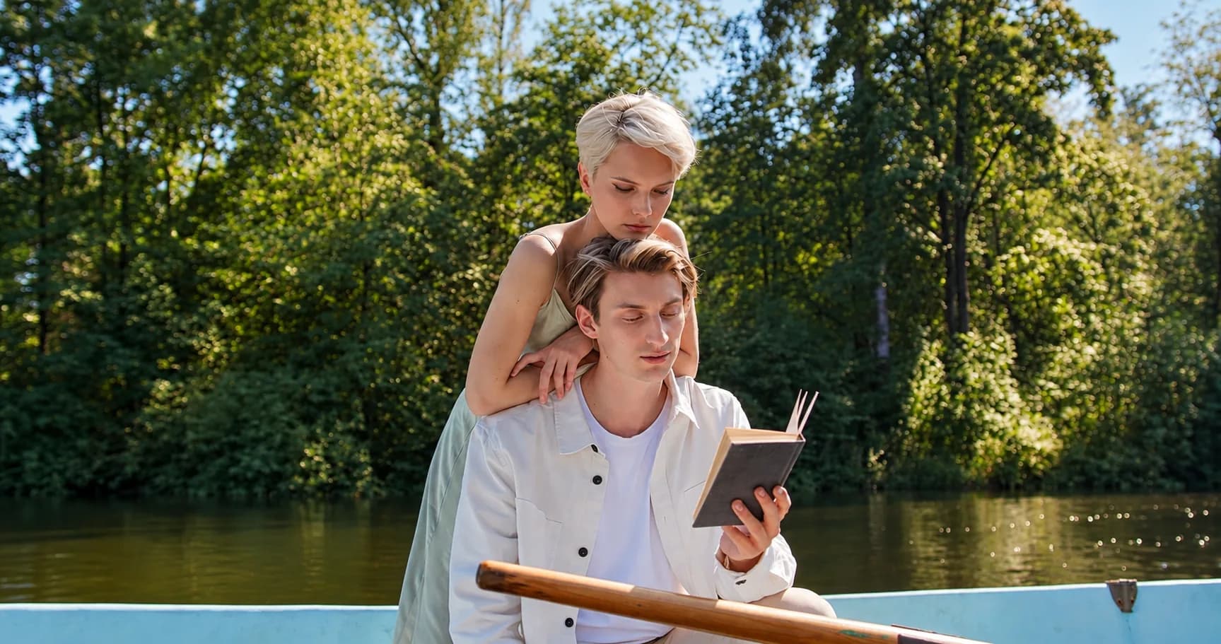 Dans une barque, au bord de l'eau, un jeune homme lit un livre à voix haute, une femme penchée sur son épaule